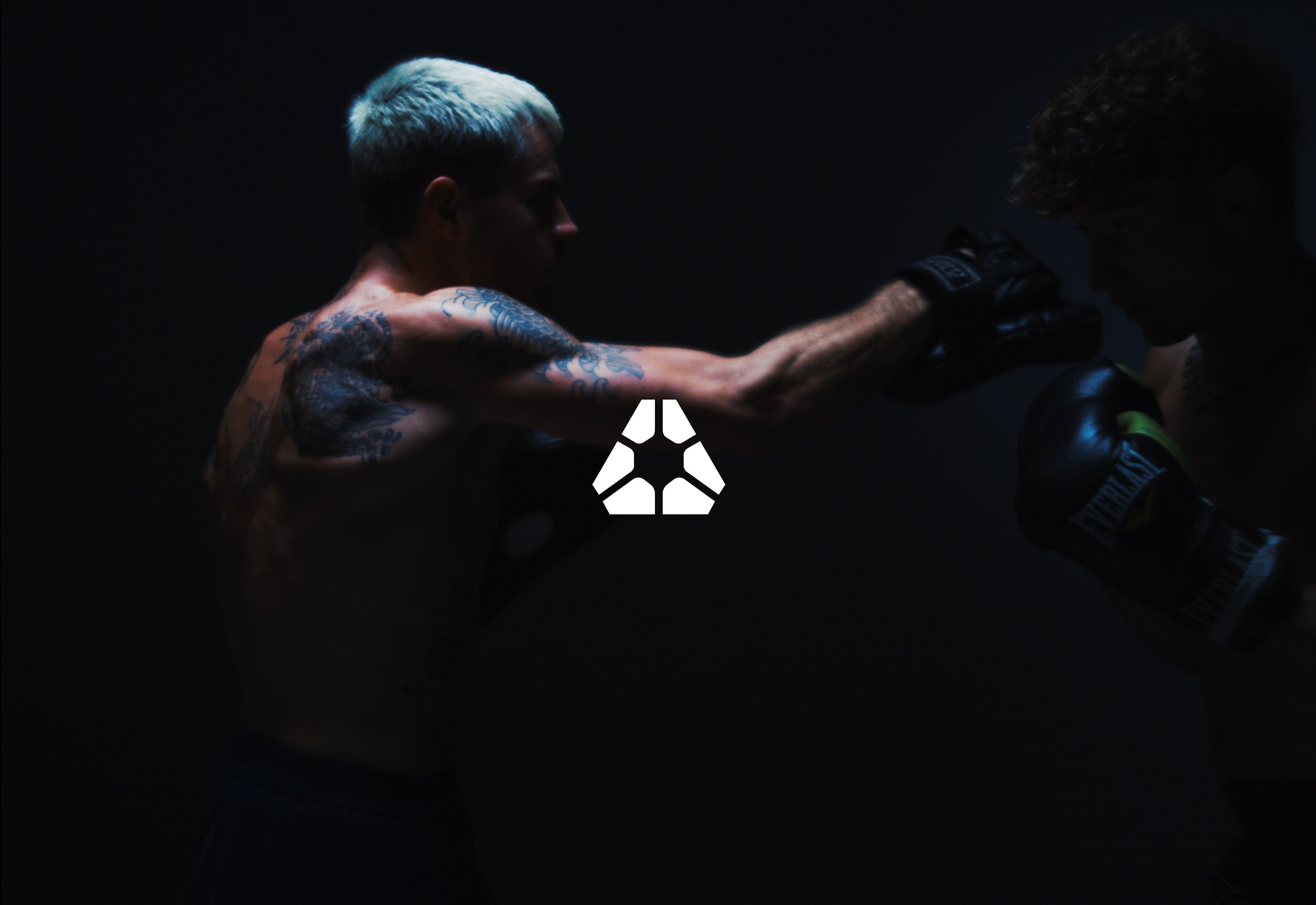 Two boxers sparring in a dimly lit room, one with tattoos.