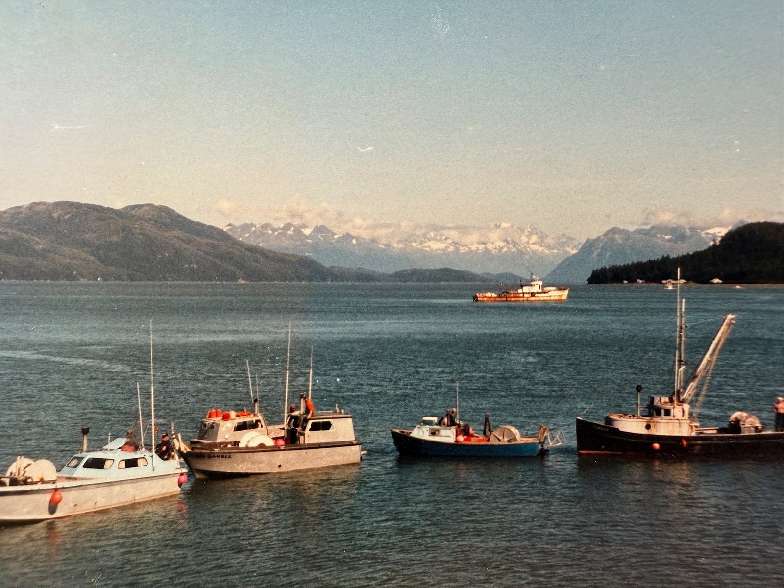 Fishing boats on water in Alaska with mountains in the background
