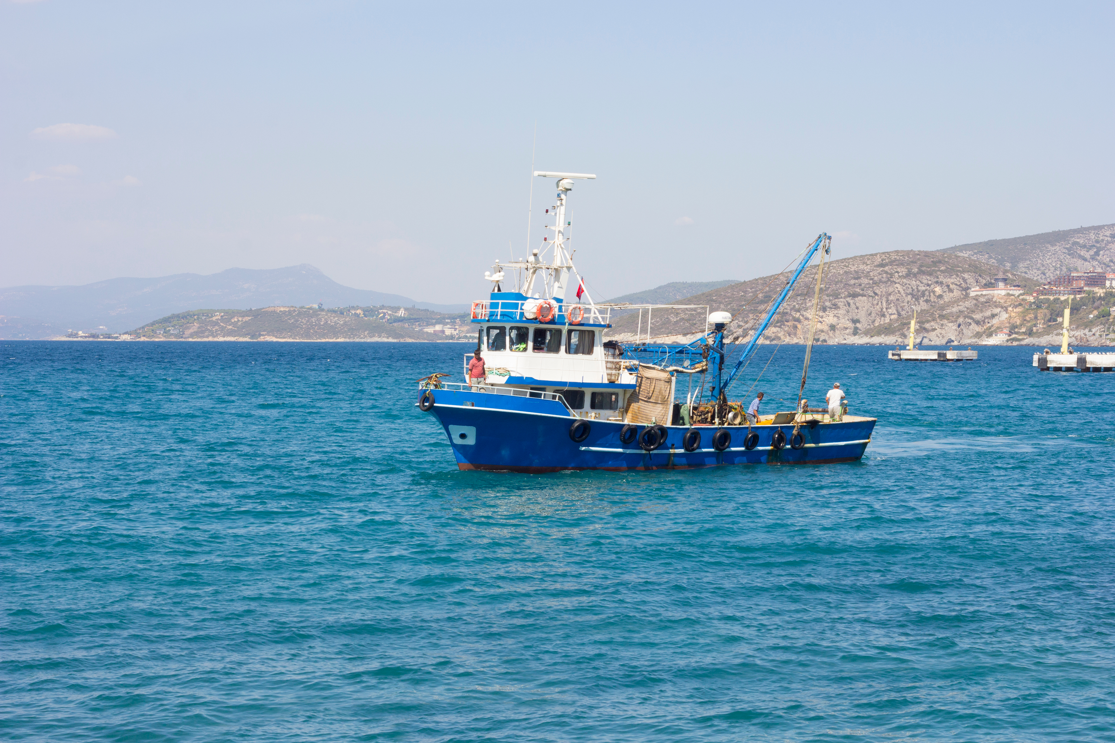 A blue fishing boat on the sea with distant hills in the background.