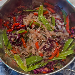Stir-fried vegetables and noodles in a pan, including snow peas and red peppers.