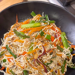Stir-fried noodles with vegetables in a black bowl.