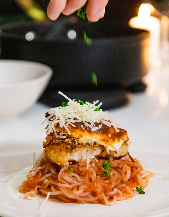 Hand sprinkling herbs on pasta with cheese and sauce.
