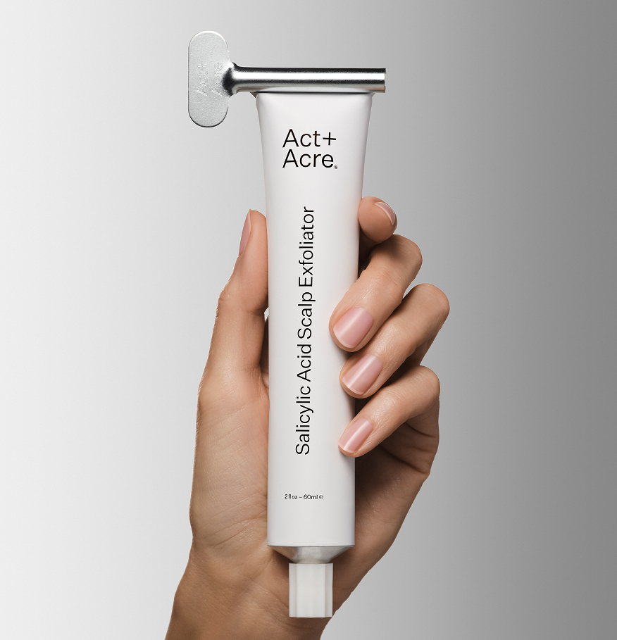 Hand holding a tube labeled 'Salicylic Acid Scalp Exfoliator' by Act+Acre.