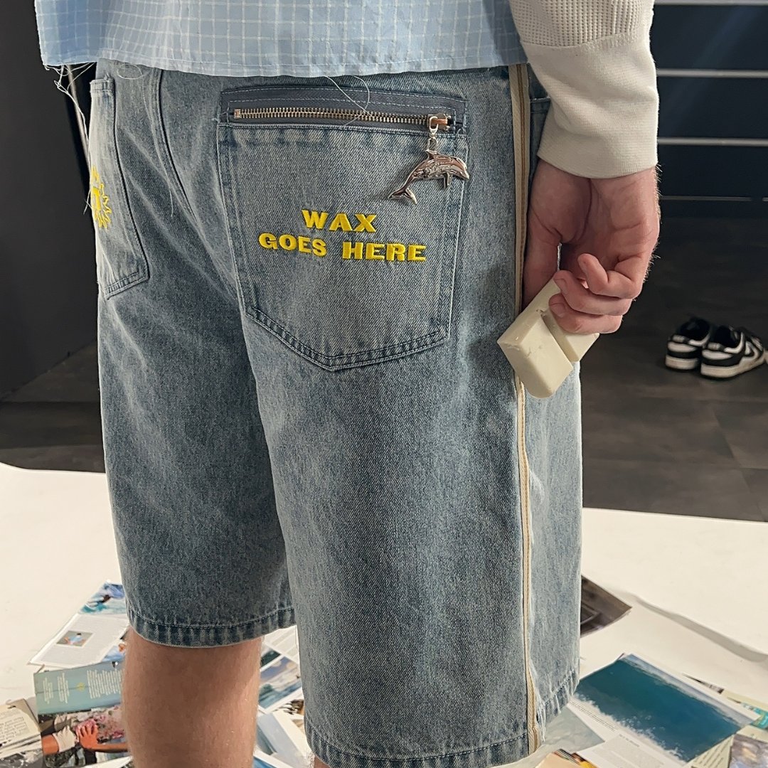 Person wearing denim shorts with 'WAX GOES HERE' text, holding a bar of wax.