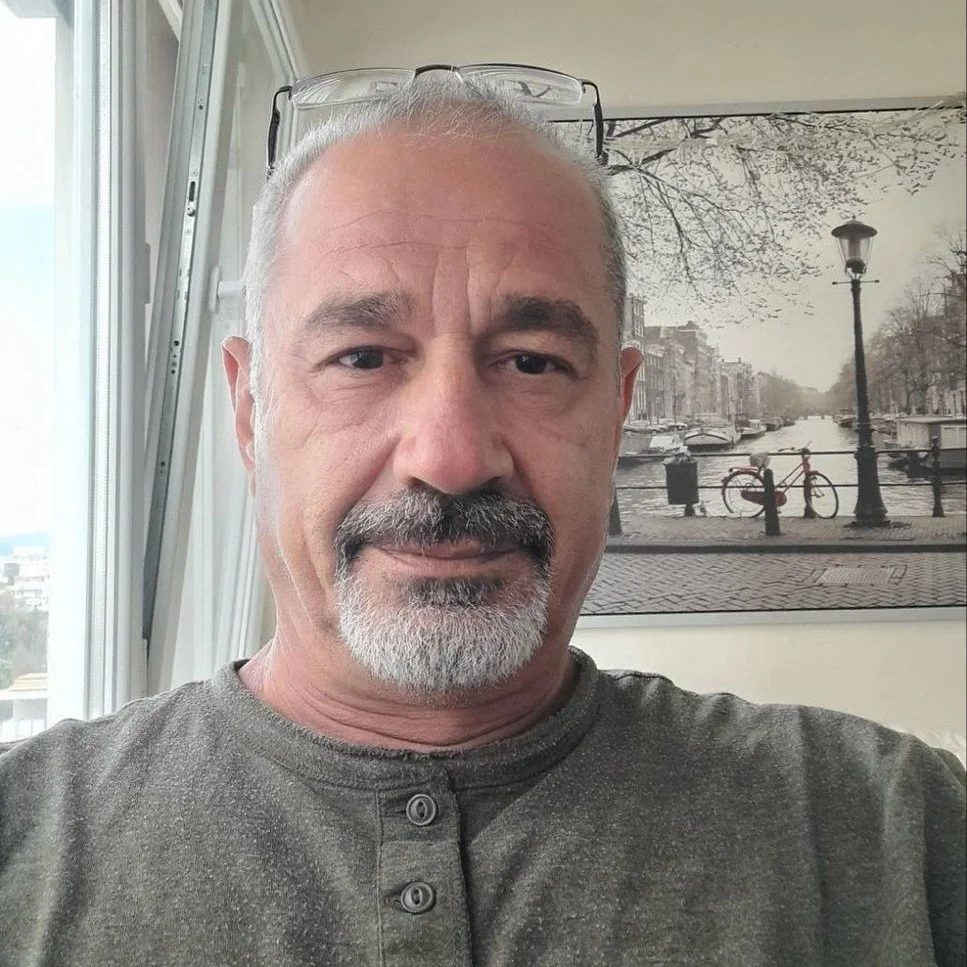 A middle-aged man with gray hair and a goatee, wearing glasses on his head, looks at the camera.