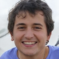 A headshot of a smiling person with short, dark, wavy hair wearing a purple t-shirt.