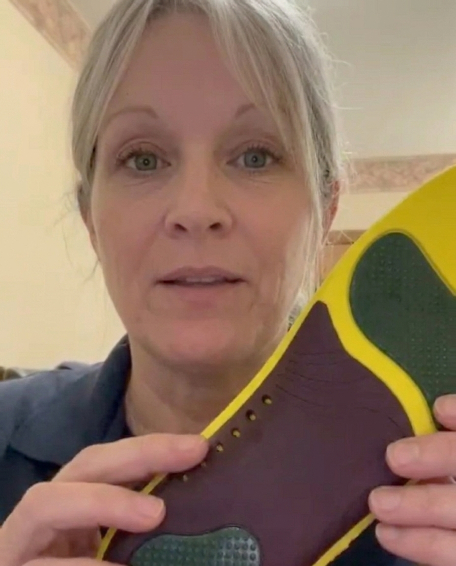A woman with blonde hair and green eyes holds up a yellow and purple shoe insole.