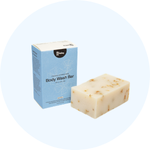 A textured, off-white bar of soap sits next to its light blue and white cardboard packaging box.