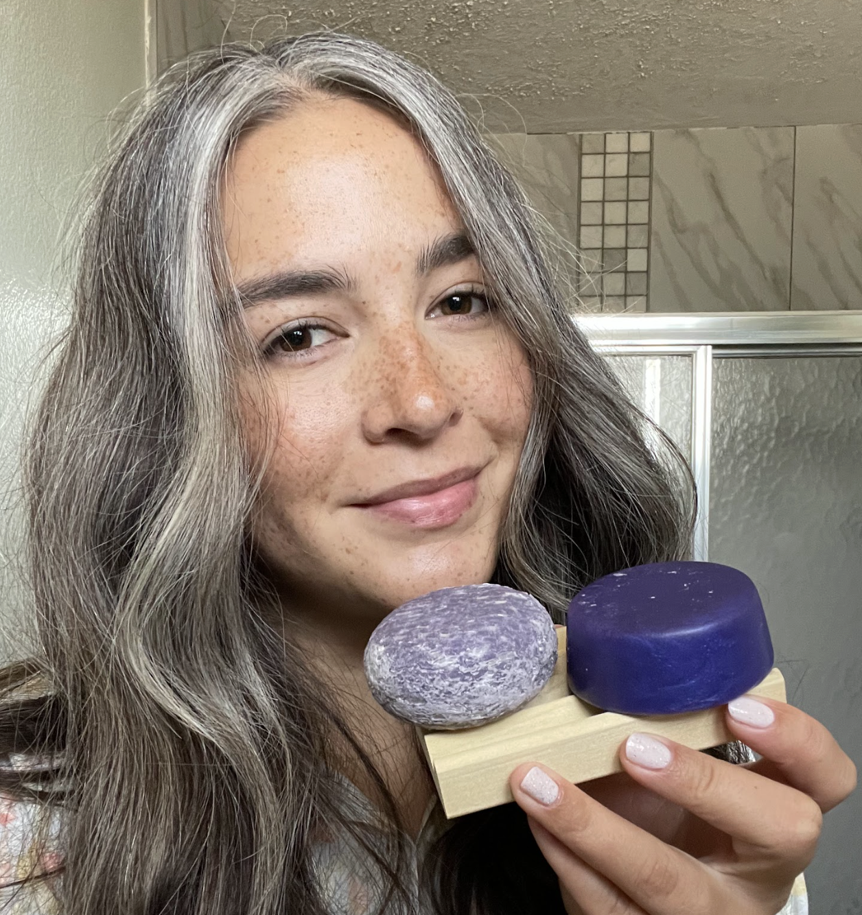 Person holding two purple soap bars on a wooden dish.