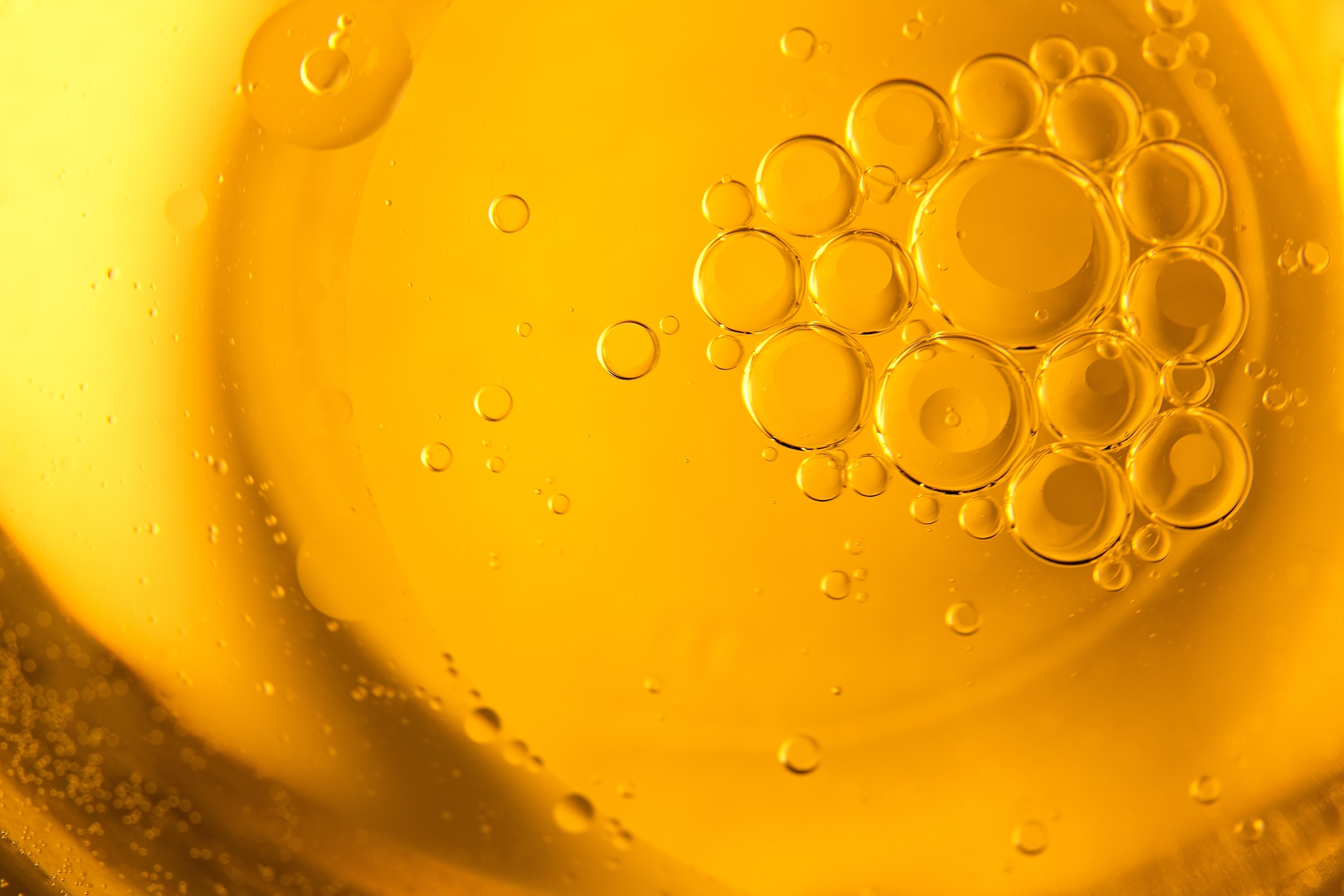 A close-up photograph of bubbles of varying sizes in a golden-yellow liquid.