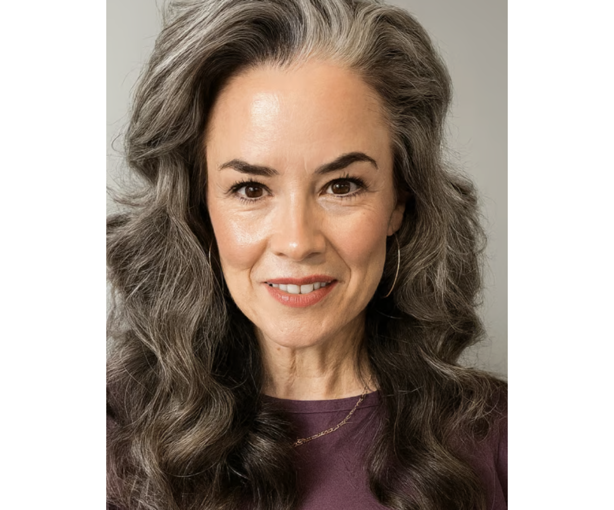 A person with wavy gray hair smiling, wearing a purple top.