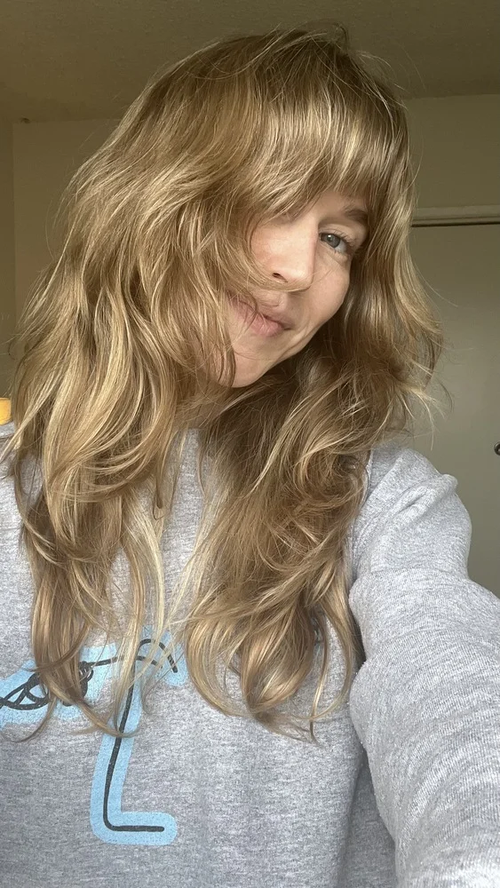 Person with long, wavy blonde hair wearing a gray sweatshirt.