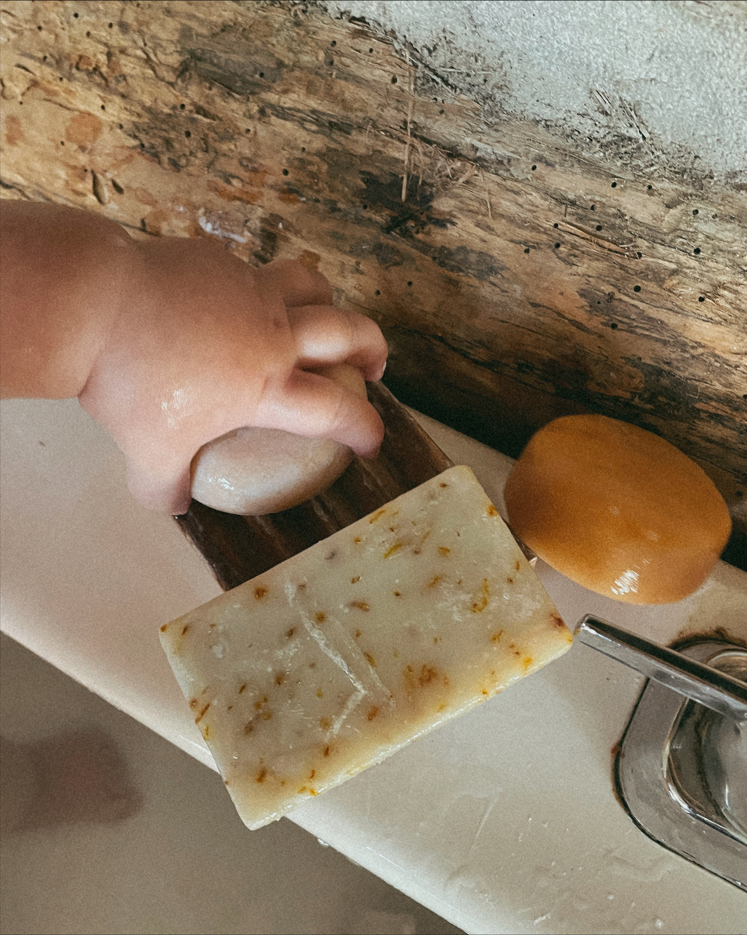 Hand holding bar of soap on soap dish by rustic wooden surface.