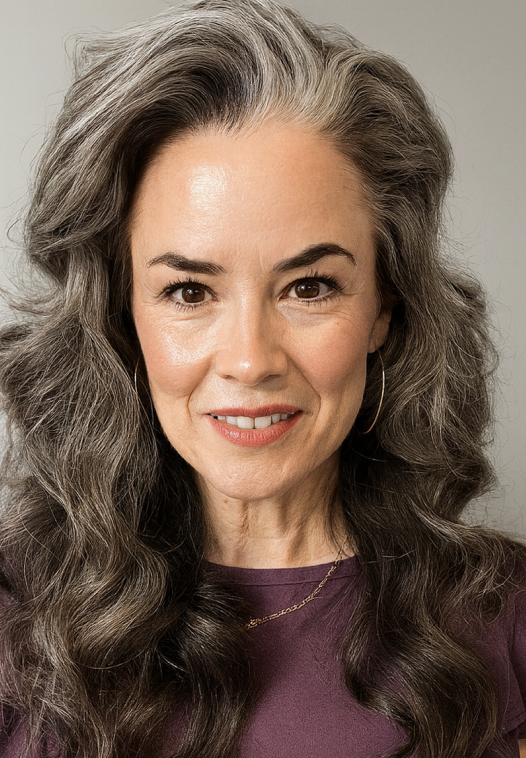 Woman with long wavy gray hair and a purple top, smiling.