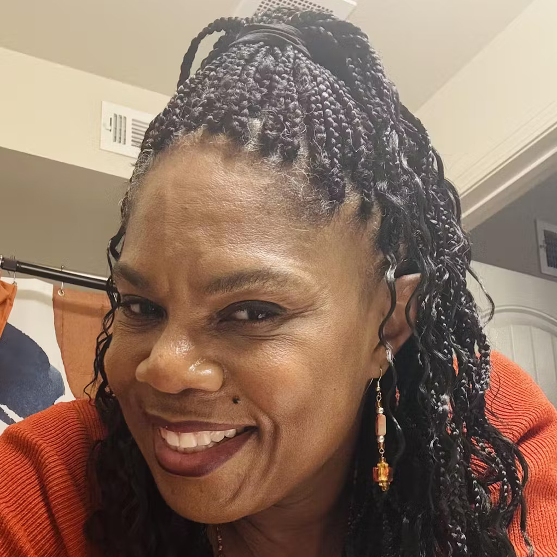 Smiling person with braided hair and earrings in a bathroom.