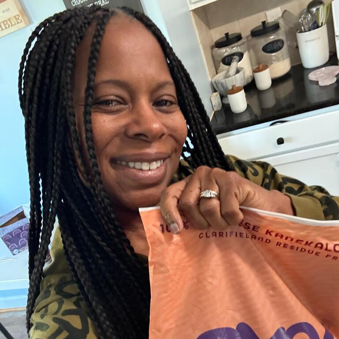 Smiling person holding an orange bag in a kitchen setting.