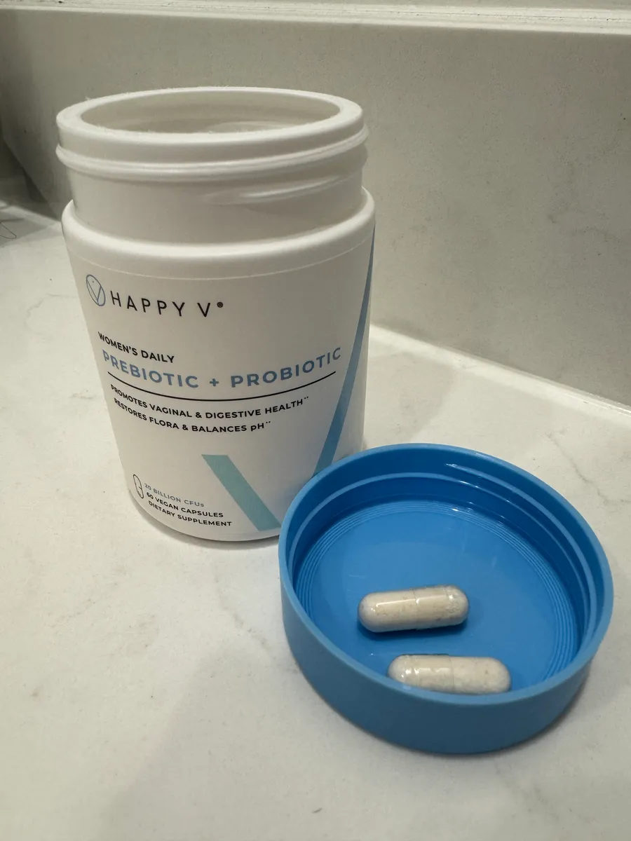 Supplement container with two capsules in a blue lid on a countertop.