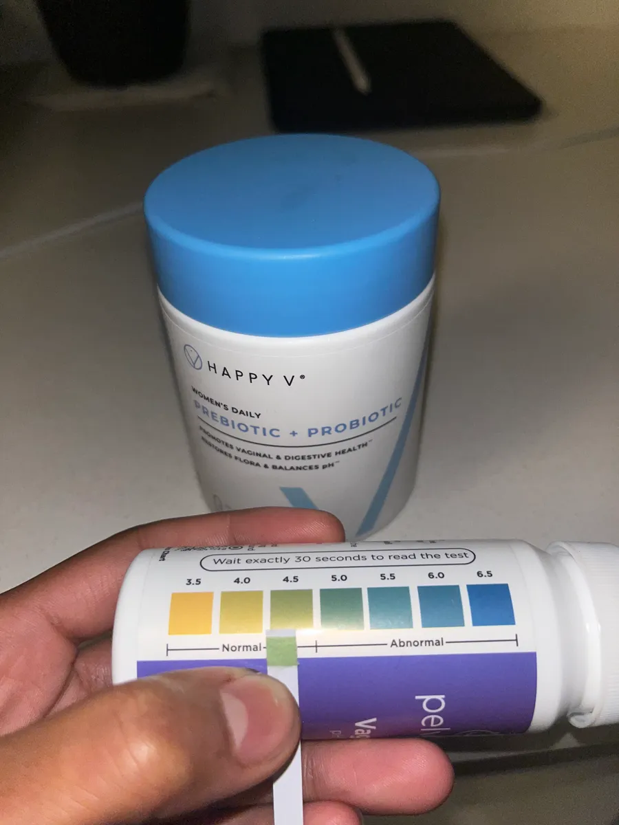 Hand holding a pH test strip against probiotic supplement bottle.