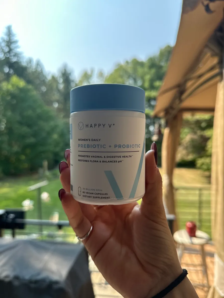 Hand holding a container of prebiotic and probiotic supplement outdoors.
