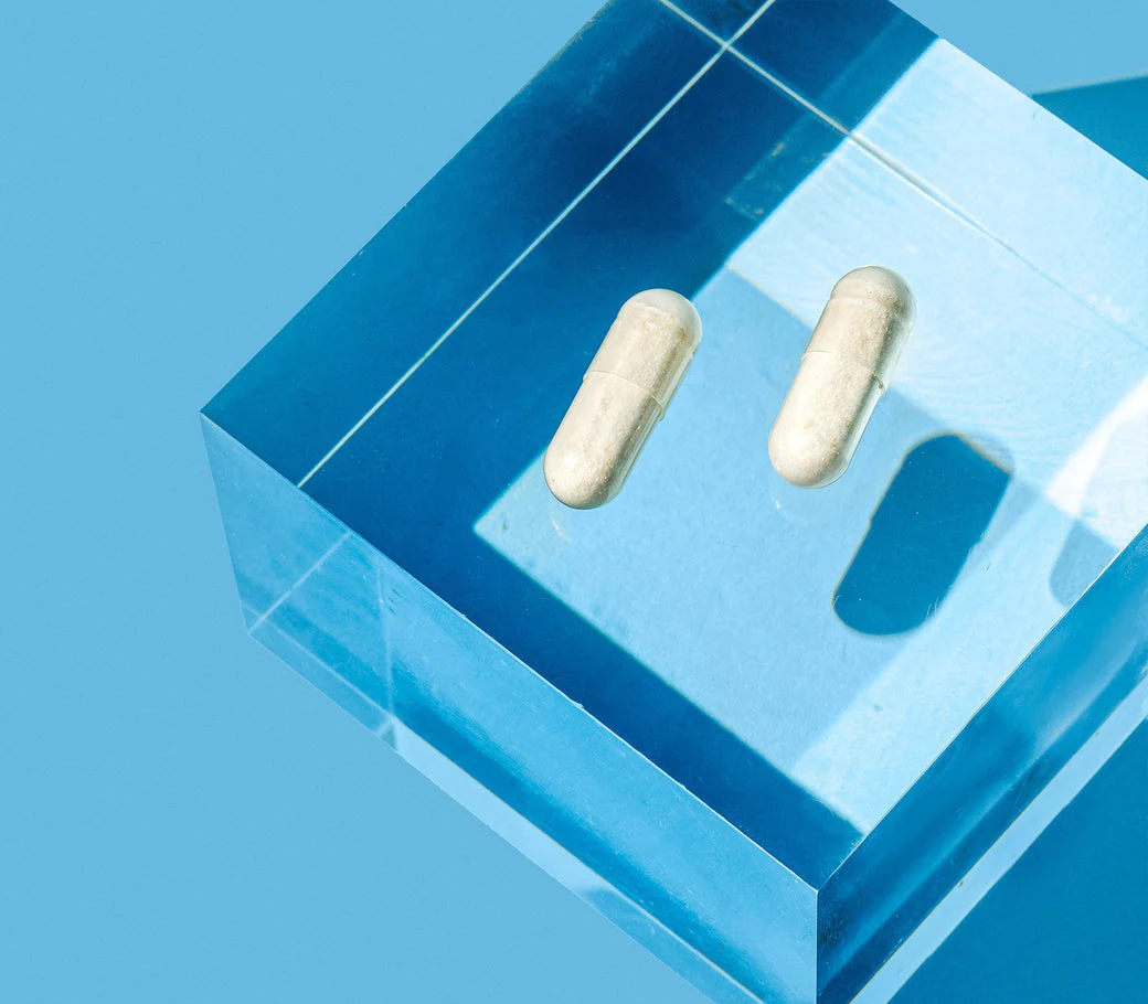 Two white capsules on a blue, transparent block against a blue background.