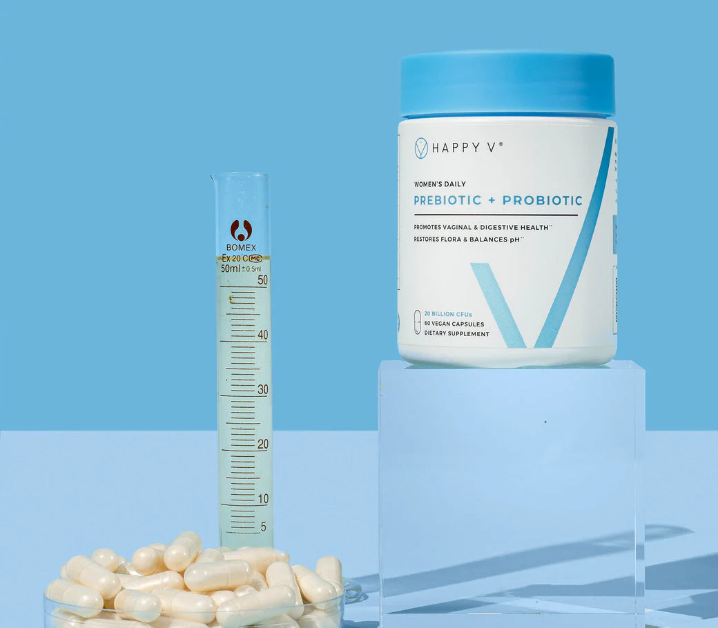 Container of prebiotic and probiotic capsules beside a beaker on a blue background.
