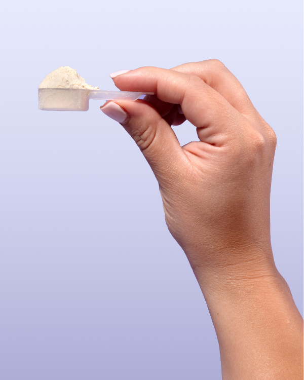 A hand holding a small plastic scoop filled with a light-colored powder against a purple background.