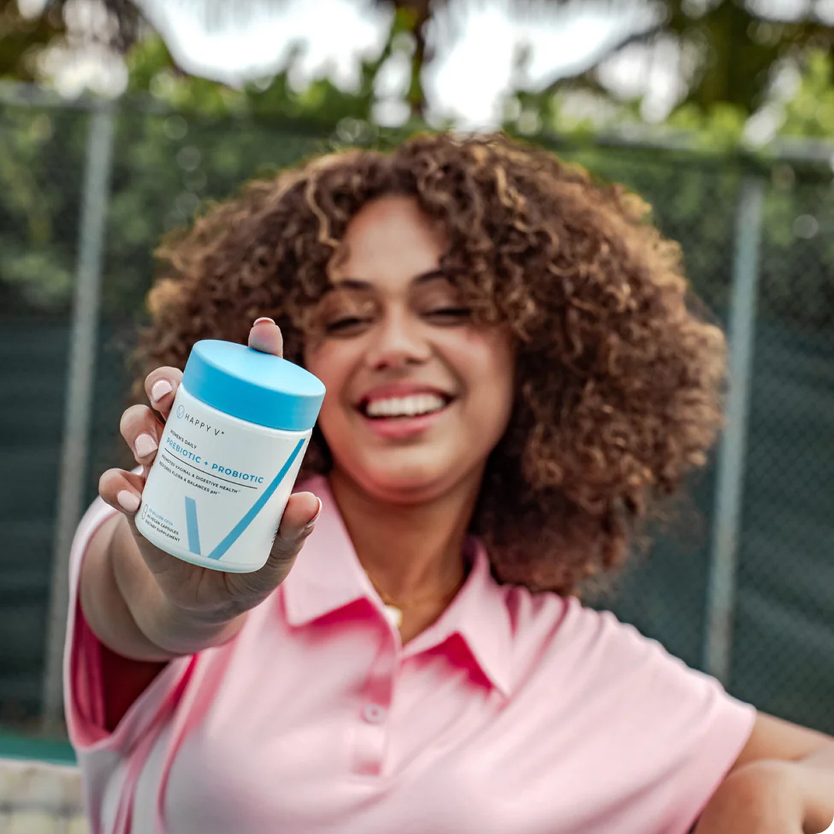 Smiling person holding a bottle labeled 'Prebiotic + Probiotic' outdoors.