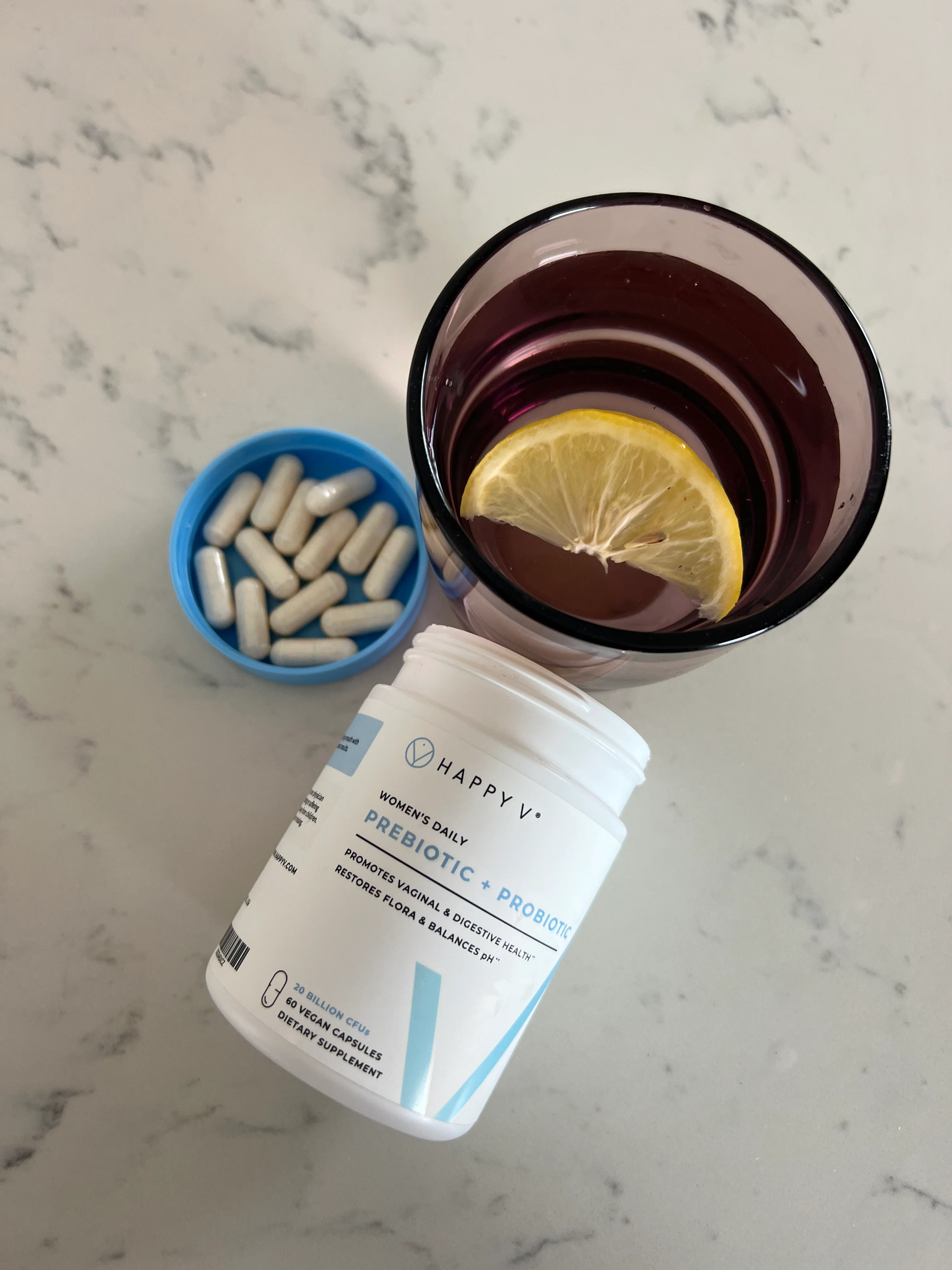 Prebiotic supplement bottle, a glass with lemon slice, and a container of capsules.