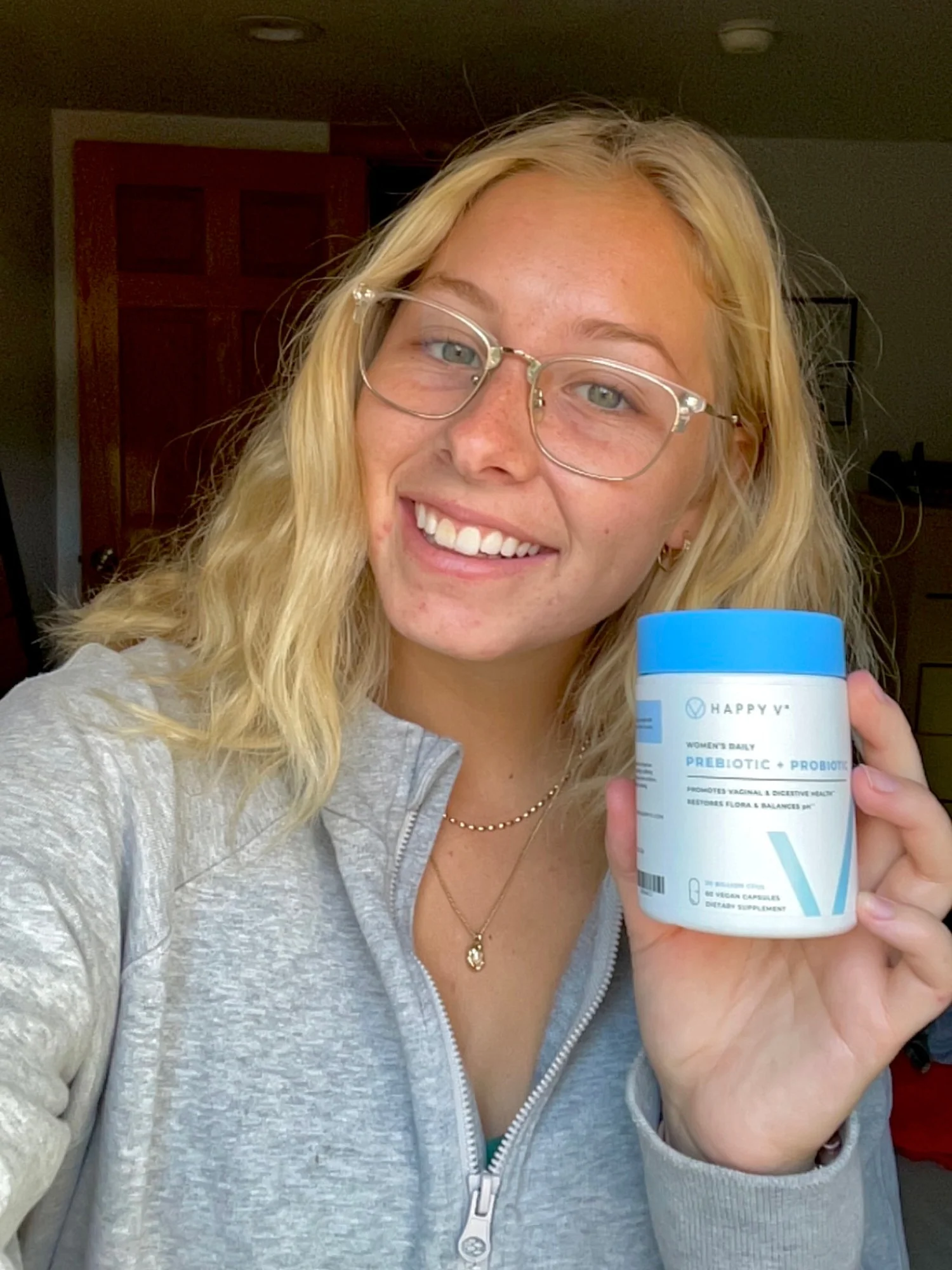A person smiling and holding a container of Happy V prebiotic and probiotic supplement.
