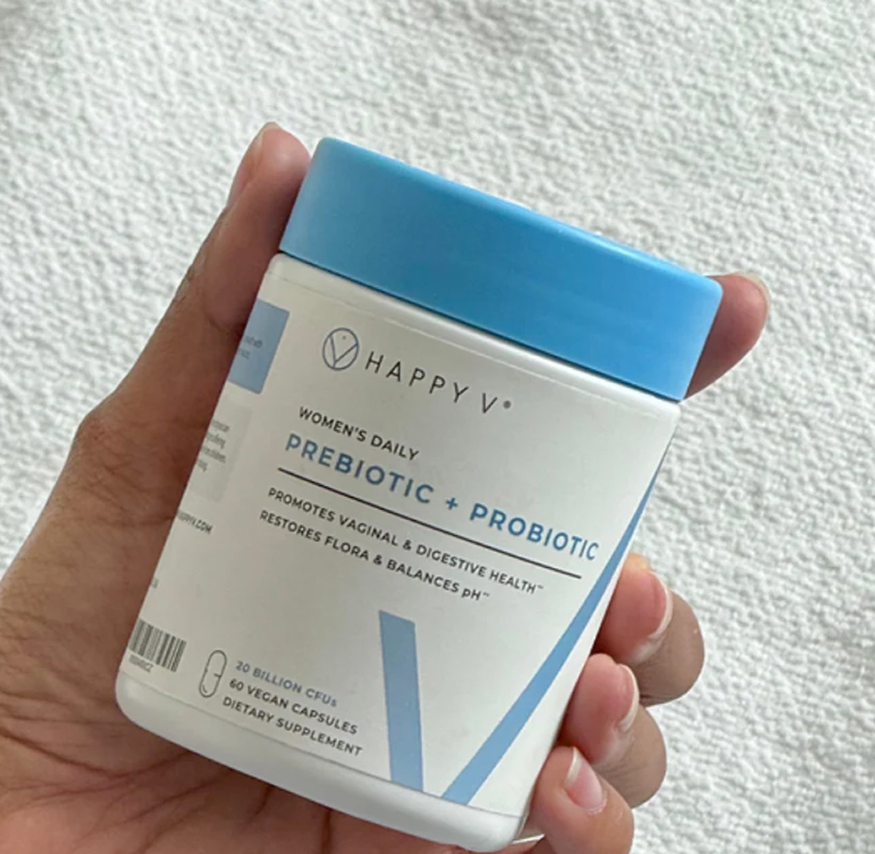Hand holding a container labeled Happy V Prebiotic + Probiotic.
