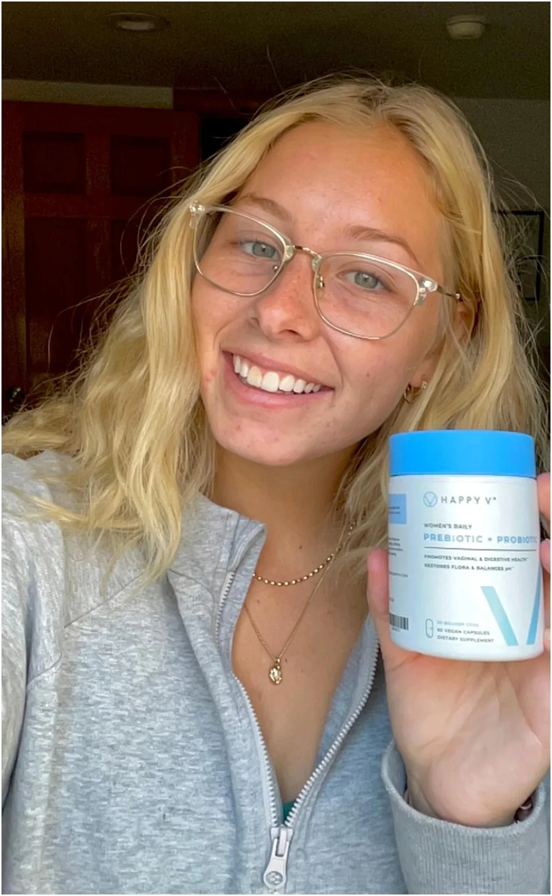 Smiling person holding a container labeled 'Women’s Daily Prebiotic + Probiotic'.