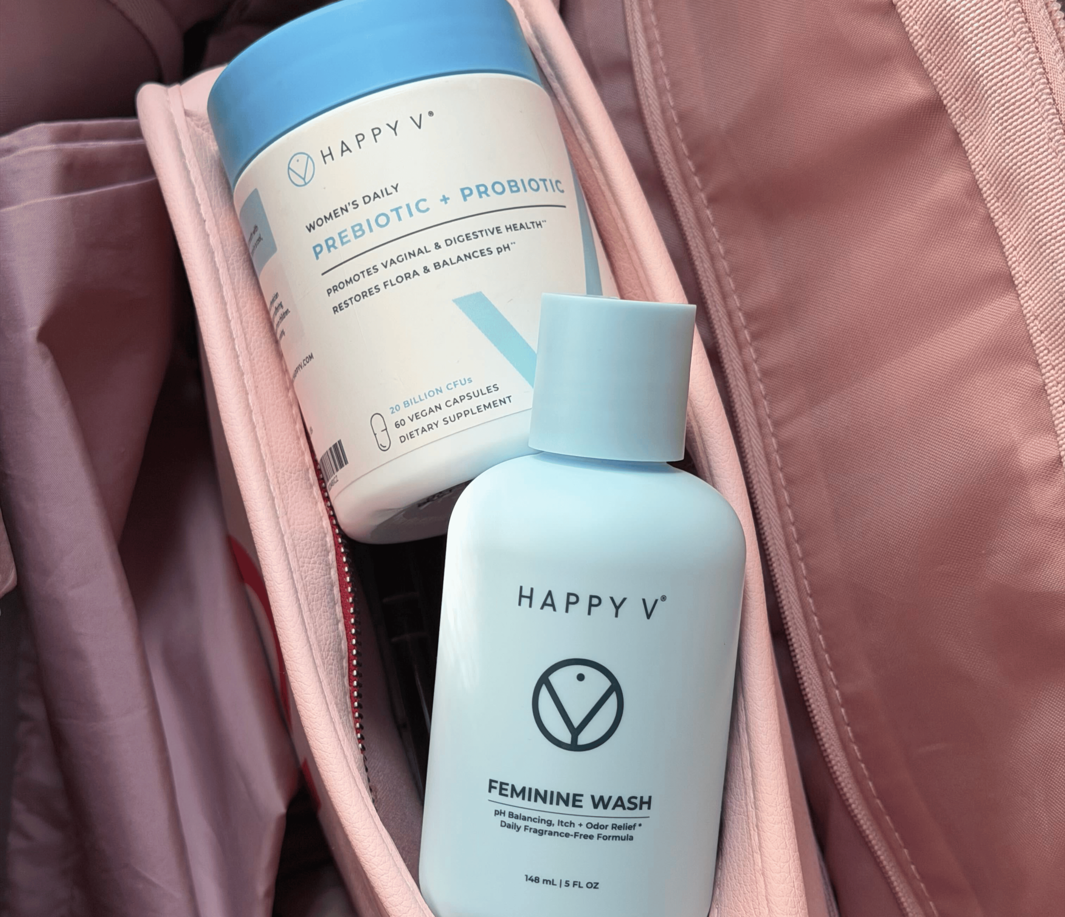 Happy V Prebiotic + Probiotic capsules and Feminine Wash bottles sitting in an open pink bag.