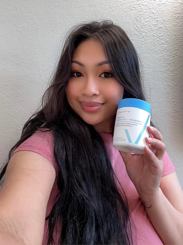 Person holding a container of prebiotic and probiotic supplement, smiling at the camera.