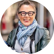 Person smiling with glasses and a scarf, outdoors.