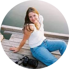 Person sitting on a wooden deck by water, with a camera beside them.