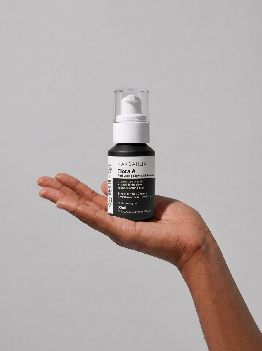 A hand holds a bottle of Maxdahlia Flora A Anti-Aging Night Moisturizer against a plain background.