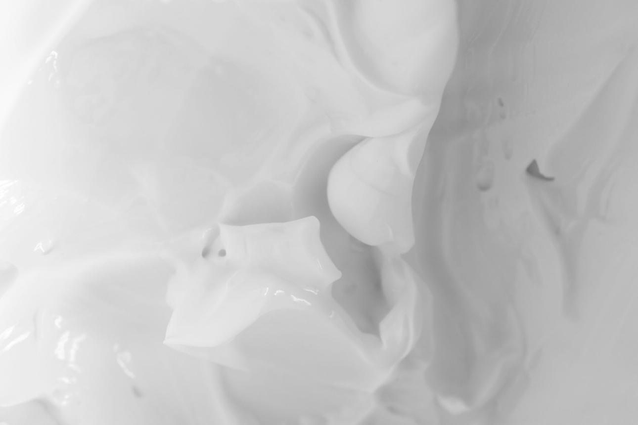 A close-up, black and white photograph showing the thick, swirled texture of a white cream.