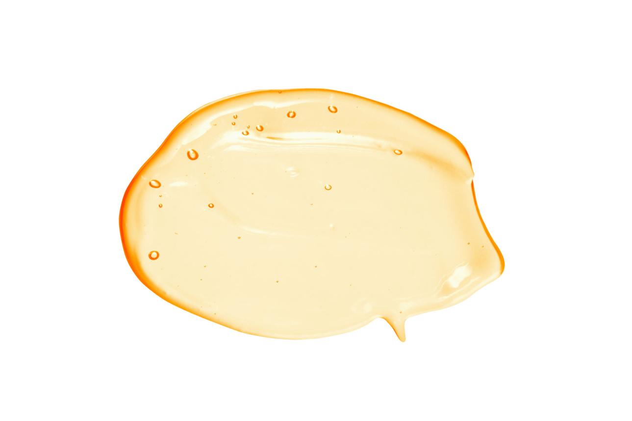 A close-up smear of a translucent, golden-yellow viscous liquid with bubbles on a white background.