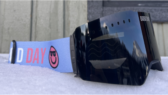 Black ski goggles with a blue strap on a snowy surface.