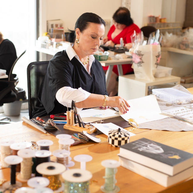 Woman working at a craft table with spools of thread and tools.