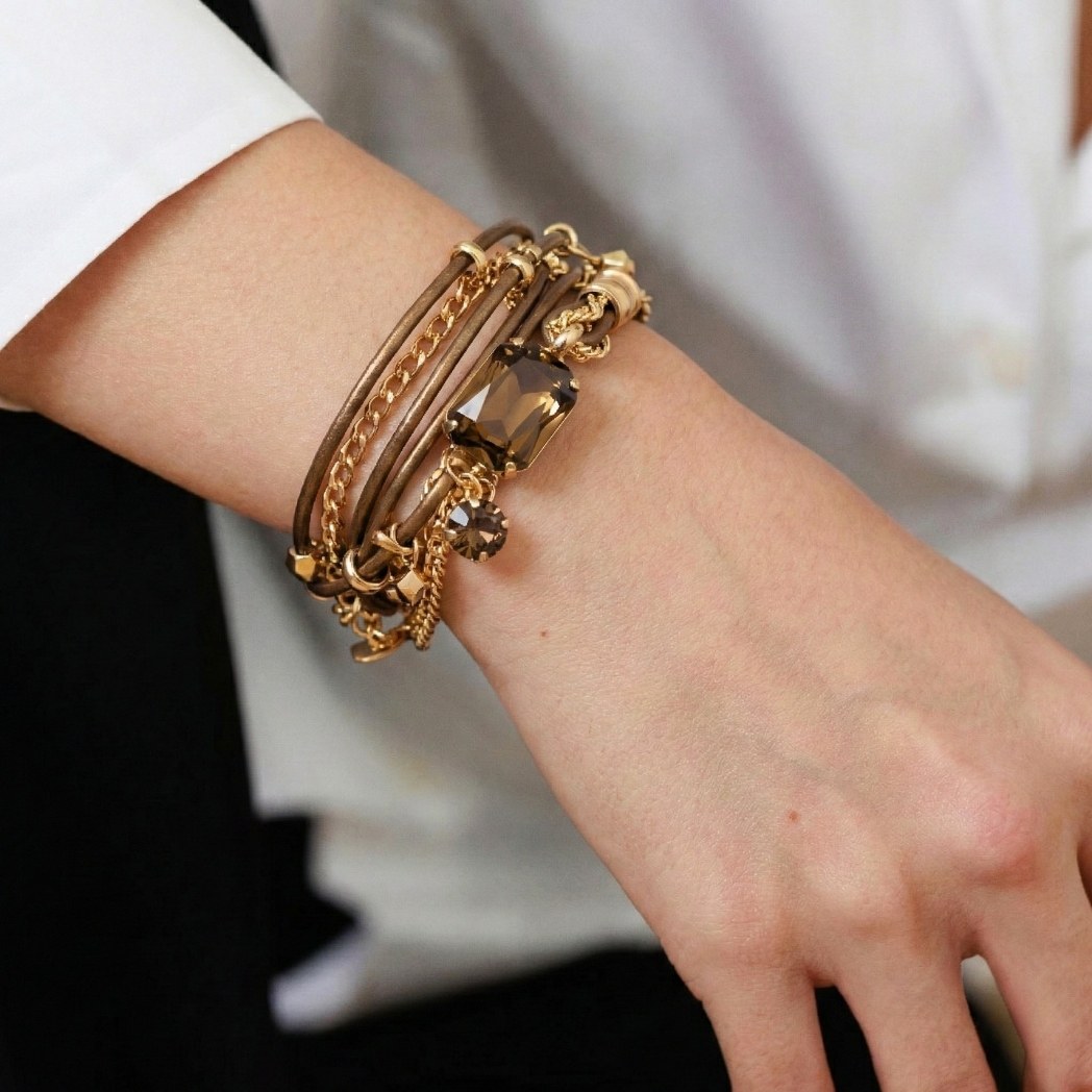 A close-up of a wrist wearing a multi-layer brown and gold bracelet with large gemstones.