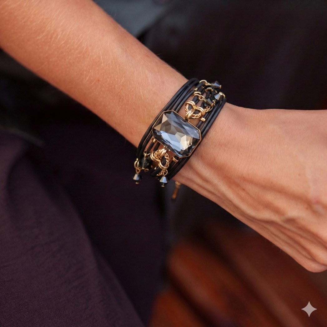 A close-up of a wrist wearing a black multi-strand bracelet with a large grey gem and gold details.
