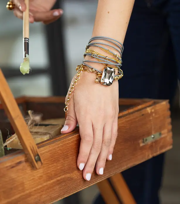 A close-up of a wrist wearing a multi-layer brown and gold bracelet with large gemstones.