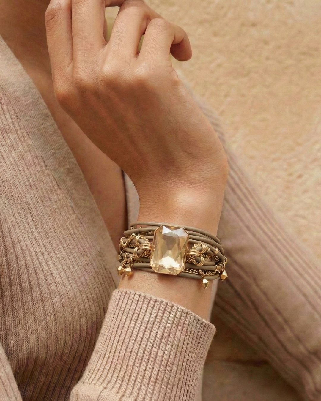 A close-up of a person's wrist wearing a wide, multi-strand bracelet with a large rectangular gemstone.