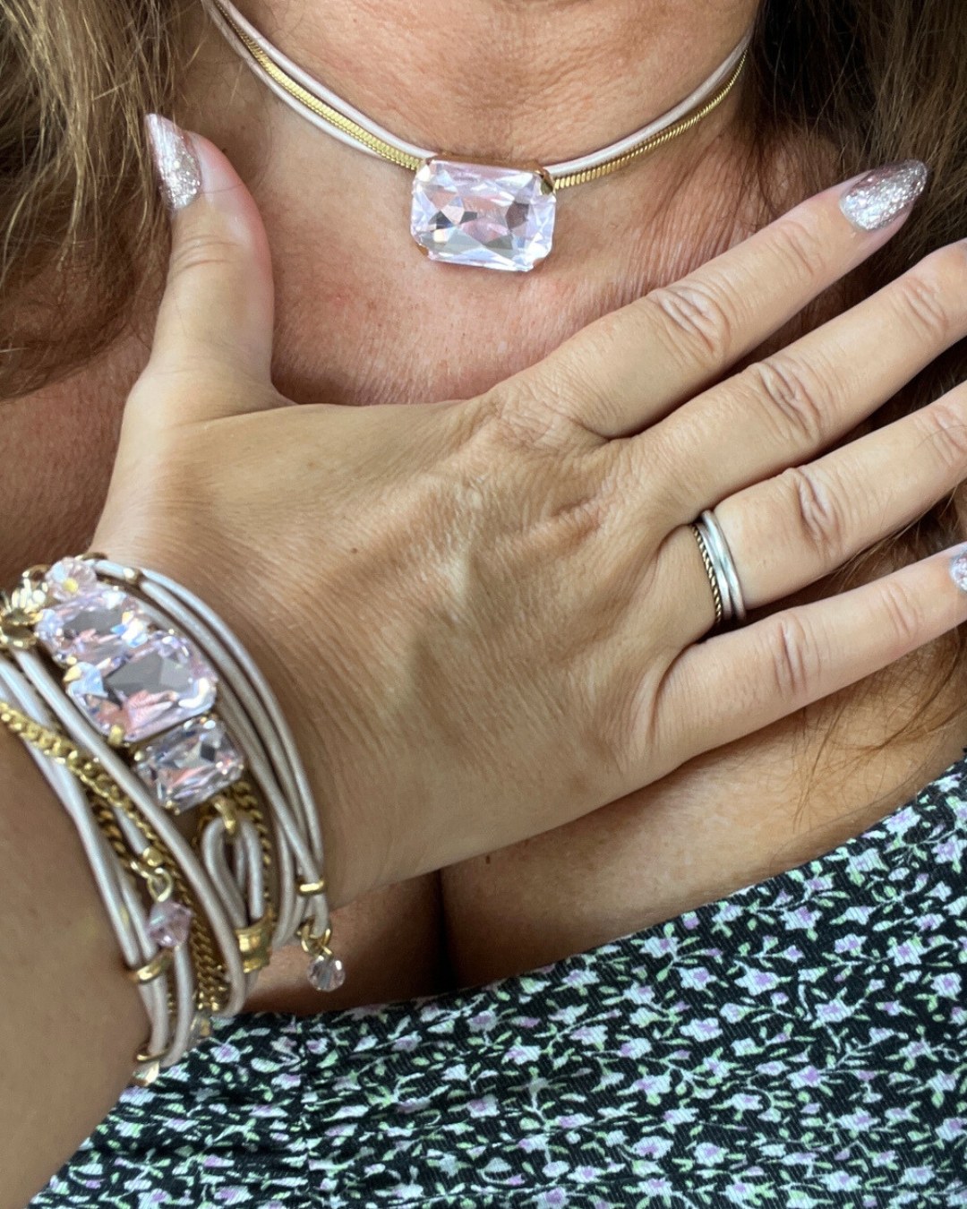 A close-up of a woman wearing a large crystal choker and matching bracelet, with glittery silver nails.