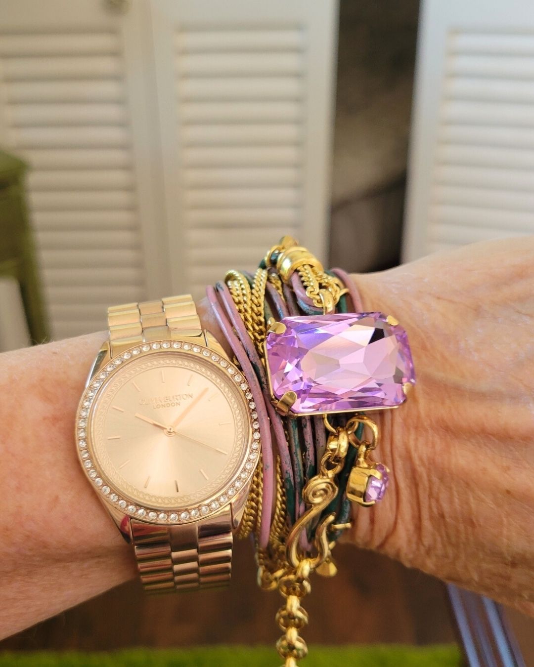 A close-up of a wrist wearing a gold watch and a colorful multi-strand bracelet with a large purple gem.
