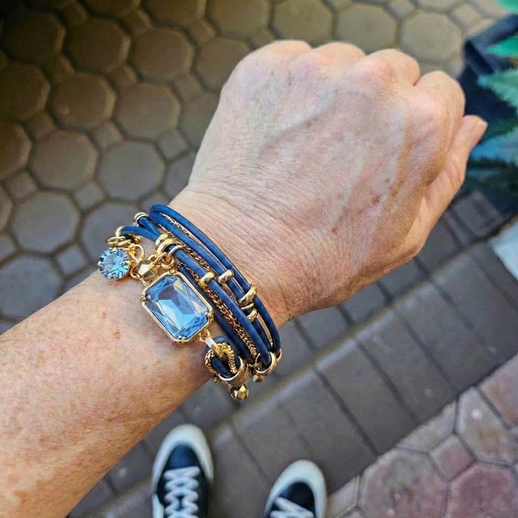 A person's wrist wearing a multi-strand blue and gold bracelet with large, light blue gemstone charms.