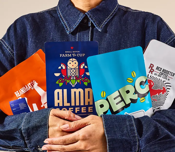 Closeup image of a person in a jean jacket holding 4 different coffee bags in their arms.