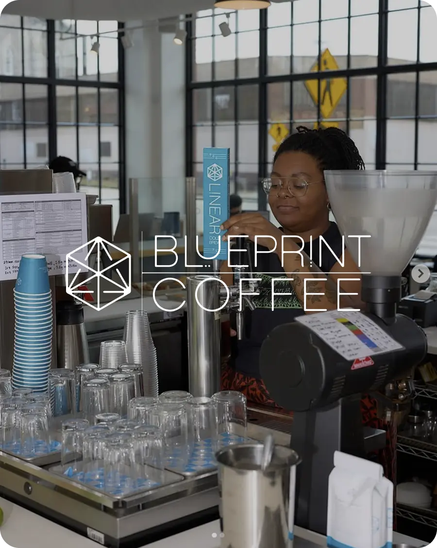 A barista at a Blueprint cafe is behind the counter and is pouring cold brew from a tap. The Blueprint Coffee logo is overlayed.