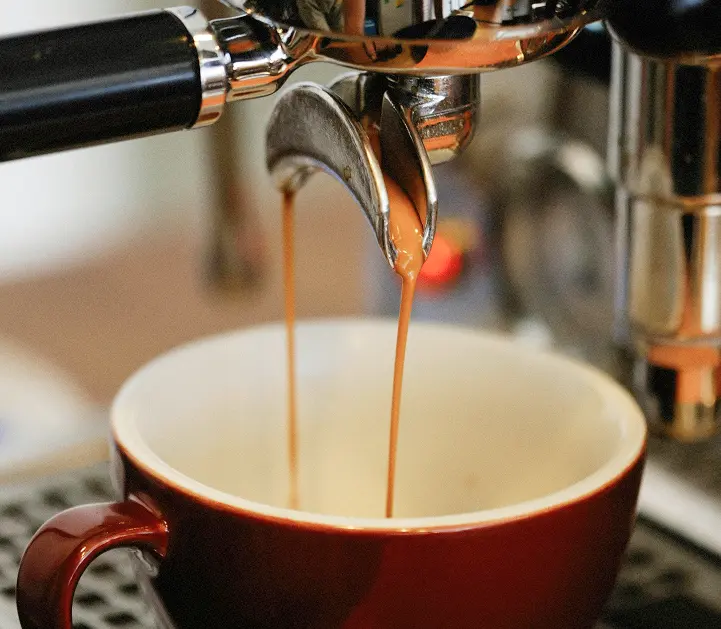 Close up of espresso pouring out of a portafilter into a mug.